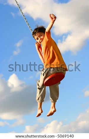 Young boy on chain swing raising one arm in excitement being lifted high.