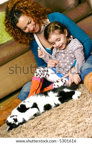 Young girl stroking the family pet cat while sitting with her mother, in a home environment
