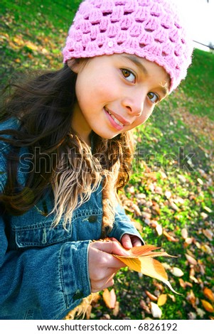 Young girl having fun collecting fallen autumn leaves in the park