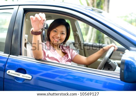 Young Asian female showing off car key while being in the driver\'s seat of a blue car.