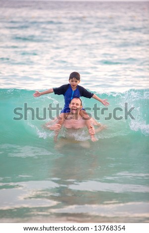 Young boy sitting on his father\'s shoulder as they got hit by big wave