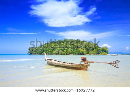 A lone tailboat waits by the shore for the tide to come in at Krabi bay, Thailand, with clear blue water against blue skies.