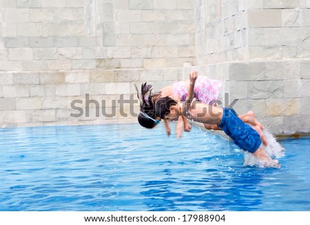 Young boy jumps in the swimming pool with sister