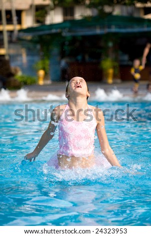 Young girl jumps out of a swimming pool with a big splash