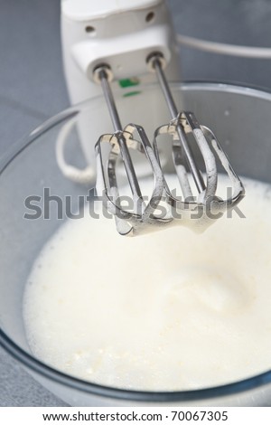 Metal egg beater with bowl of beaten eggs