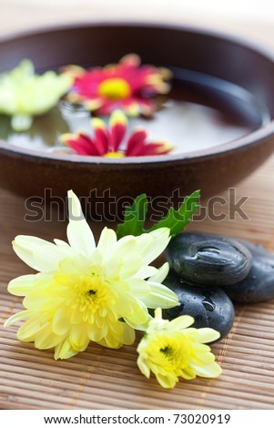 Spa setting with hot stones with chrysanthemum and bowl of water.