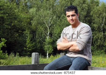 An attractive young man on his lunch hour, taking a rest in the park, sitting on a fence.