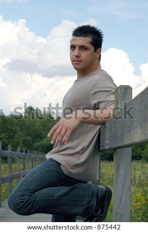 An attractive young man on his lunch hour leaning against a fence in a park.