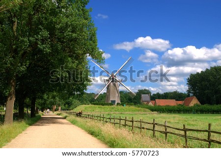 An old windmill against a blue vibrant sky along the road in Belgium. Vintage, preservation, tourism concept.