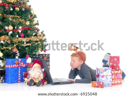 happy youngster, young boy playing with laptop next to Xmas, Christmas three with presents, gifts.  White background.