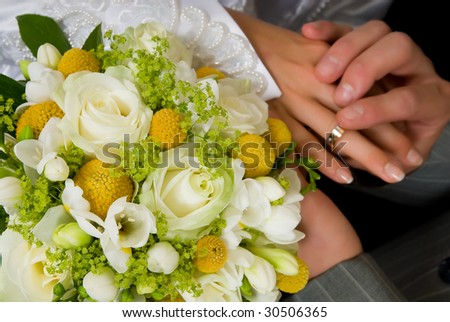 Young couple putting on wedding ring, bouquet flowers in front.  Black background, studio shot.