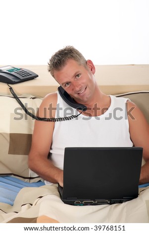 Handsome forties man making phone call  with laptop on bed in bedroom.  Studio.