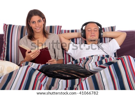 young loving couple grooming on bed in bedroom, reading book, listening music with headset.  Studio.