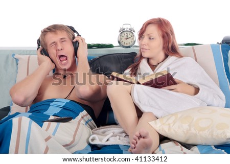 young loving couple grooming on bed in bedroom, reading book, listening music with headset.  Studio.