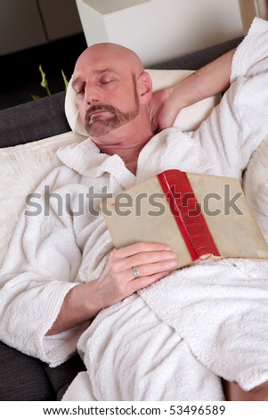 Bald Middle aged man in bathrobe at home relaxing in sofa artistic composition, shallow dof, focus on man.