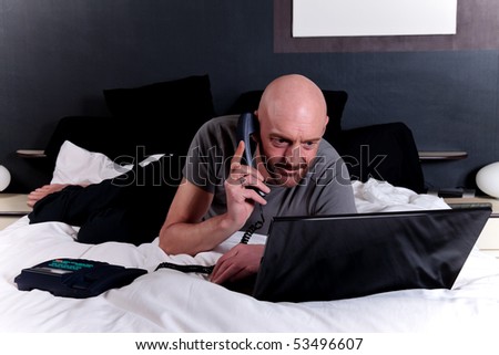Bald Middle aged man working on laptop on bed in bedroom.