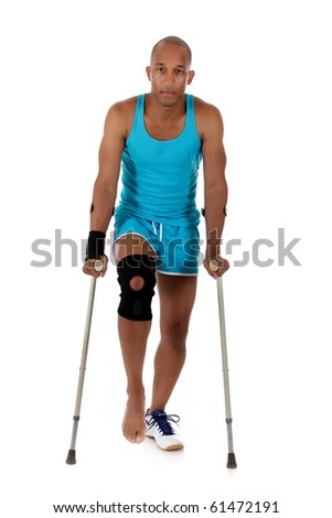 Young attractive African American man athlete on crutches, wearing a wrist brace and knee support,  bandaged. White background. Studio shot.