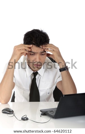 Stressed young Nepalese businessman in office at desk in front of a laptop holding his head, worried. Studio shot. White background