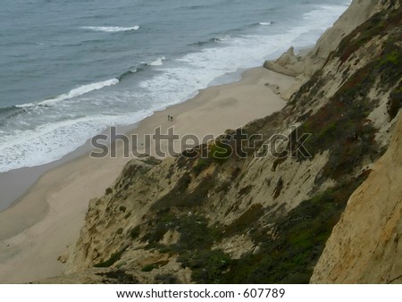 two small people on beach below cliffs