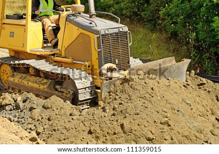 A small bulldozer moves and levels rock and dirt on a new road construction project