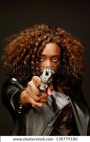A young beautiful african american female holds a semi automatic pistol during this dark photo shoot against black