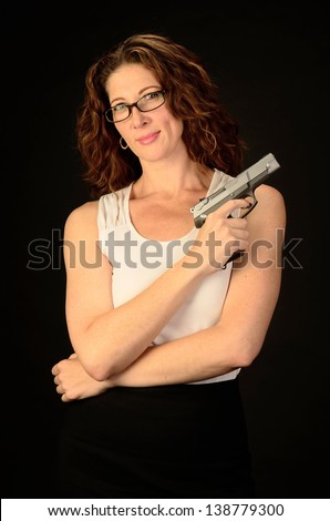 A middle aged, white, female business woman or teacher holds a semi automatic pistol during this dark photo shoot against black