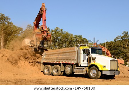 Track hoe excavator loading a 10-yard dump truck with dirt from a new commercial development construction project.