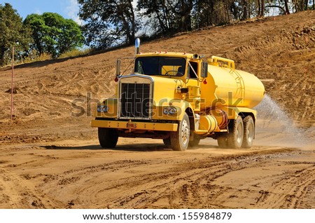 A water truck sprays water on a fresh fill layer of soil and rock for a new road construction project.