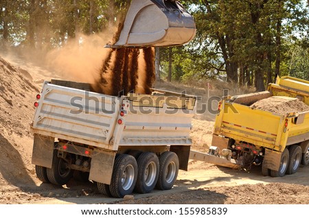 Large track hoe excavator filling a dump truck with rock and soil for fill for a new commercial development road construction project