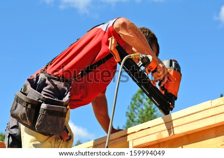 Building contractor worker with a air nail gun  nailer working on the corner of the top plate of the first floor walls on a new home constructiion project