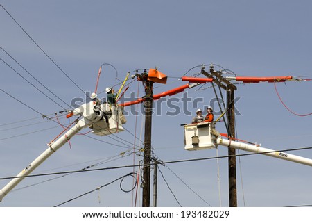 ROSEBURG, OR, USA - APRIL 29, 2014: Electrical linemen with two large boom trucks replace a wood power pole and move the voltage power lines following accident damage to the pole.