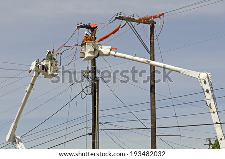 ROSEBURG, OR, USA - APRIL 29, 2014: Electrical linemen with two large boom trucks replace a wood power pole and move the voltage power lines following accident damage to the pole.