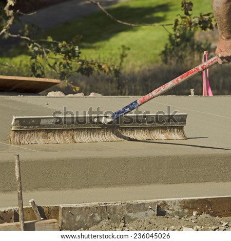 Concrete construction contractor using a broom to install texture in a sidewalk, curb and storm drainage gutter on a new urban road street project