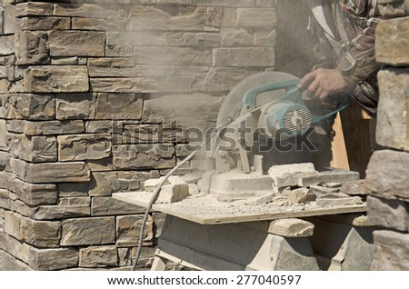 Masonry contractor using a dry circular tile or rock cutting saw to trim rock siding for a home installation