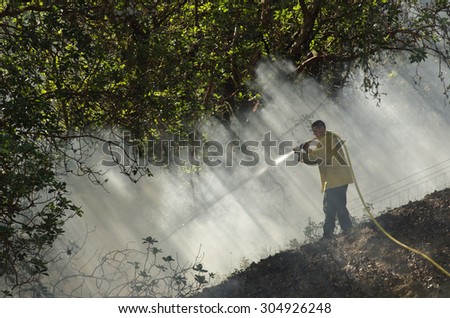 Roseburg, OR, USA - July 6, 2014: A firefighter works the edge of a wildland fire on a slope and in smoke.