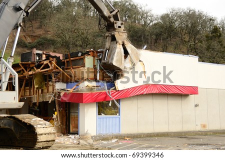 Large clamshell bucketed track hoe tearing down a former restaurant for a new commercial building project in Roseburg OR