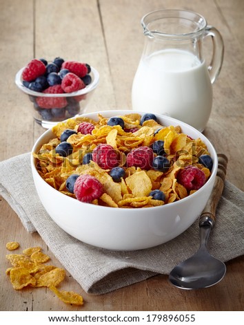 Bowl of corn flakes and fresh berries and jug of milk on  wooden background