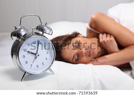 Young woman sleeping in bed with alarm clock in foreground