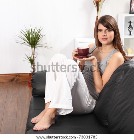 Beautiful young, caucasian woman, sitting on the sofa at home drinking coffee.