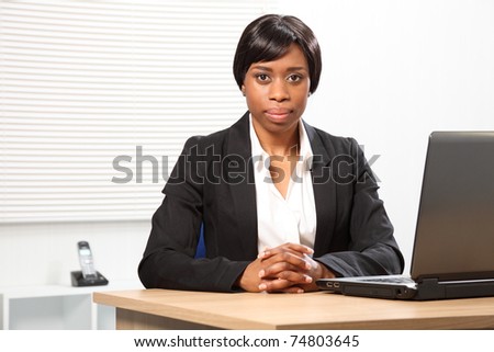 Beautiful young African American woman working in office sitting to her desk with a serious, stern expression.