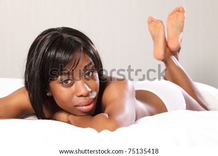 Beautiful young topless African American woman lying casually in bed, very relaxed with chin resting on her hands.