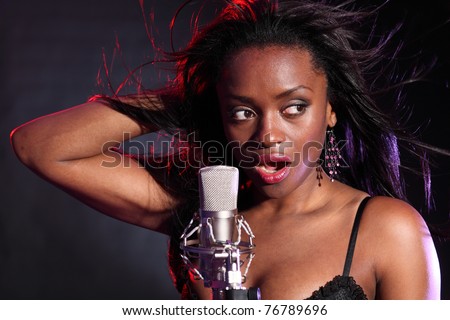 Beautiful african american girl on stage with microphone singing. Her hair is blowing back with wind effect and lit with red and blue lighting.