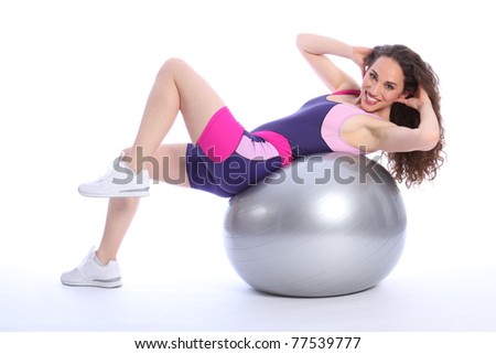 Beautiful young woman doing warm up fitness ball exercise routine. Woman has a happy smile and is wearing bright blue and pink sports clothes.