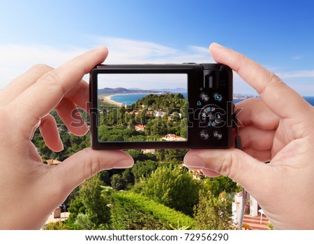 Hands holding digital photo camera while capturing summer view of private houses near the sea