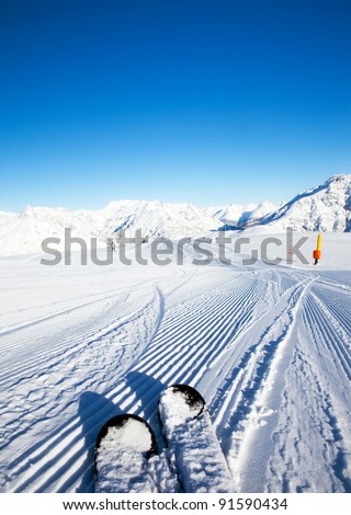 Fresh made ratrak (snowcat) snow curves under your skis and mountains panorama in the morning sunlight