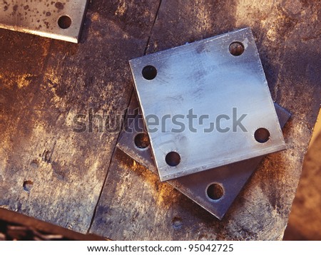 Grunge rusty rectangle metal plates with round holes placed on wooden textured board