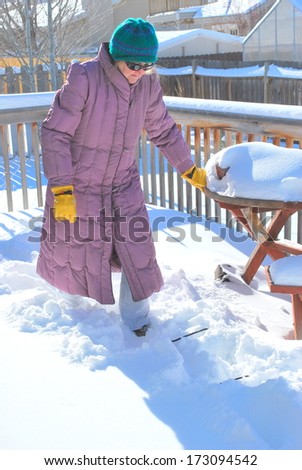 Mature female shoveling snow off her patio deck outside.