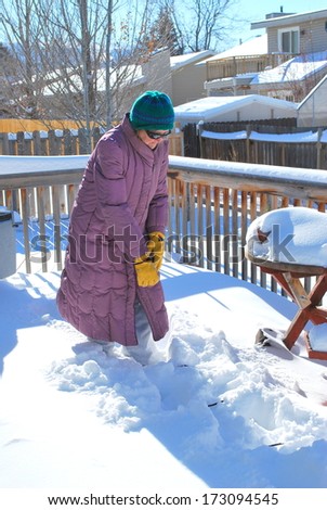 Mature female shoveling snow off her patio deck outside.