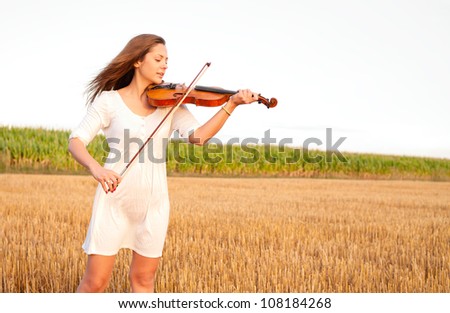 Young woman playing violin outdoors on the field in summer evening