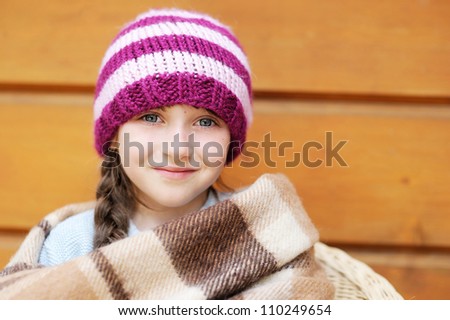 Closeup portrait of a beautiful little girl wearing knitted hat while wrapping up in plaid